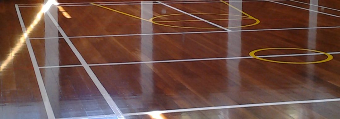 Hall of the Church complex, showing a shiny varnished wooden floor and wooden walls with painted markings for various sports: volleyball, badminton, basketball.